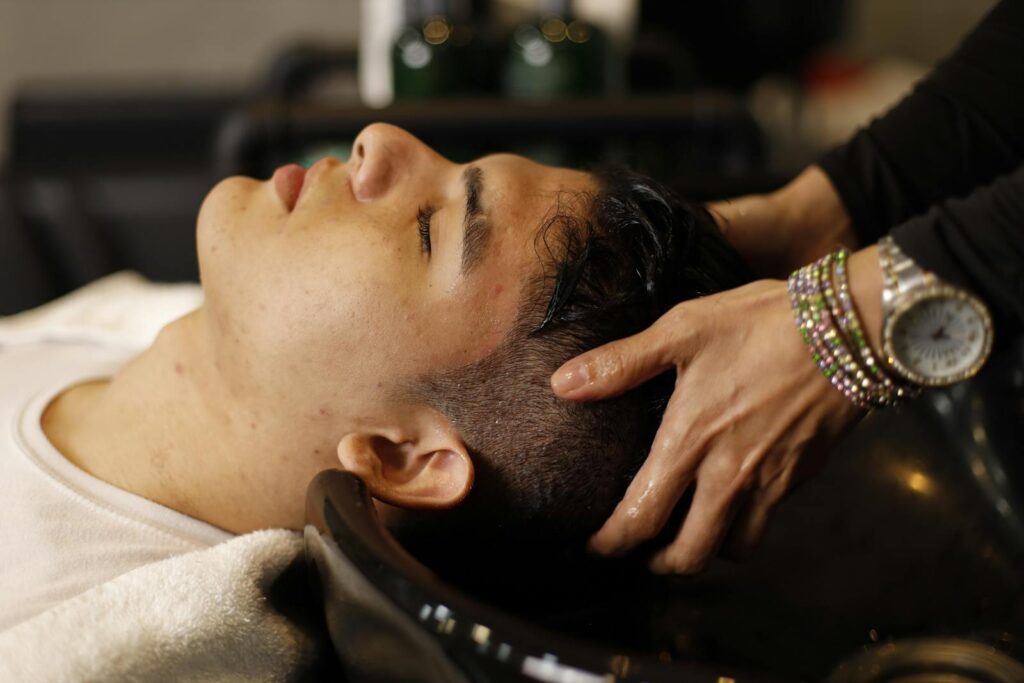 Man with closed eyes enjoying a relaxing hair wash at salon sink by a professional stylist.