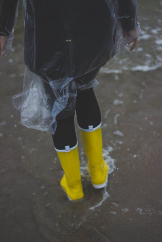 Person wearing yellow boots and raincoat, splashing through water outdoors.