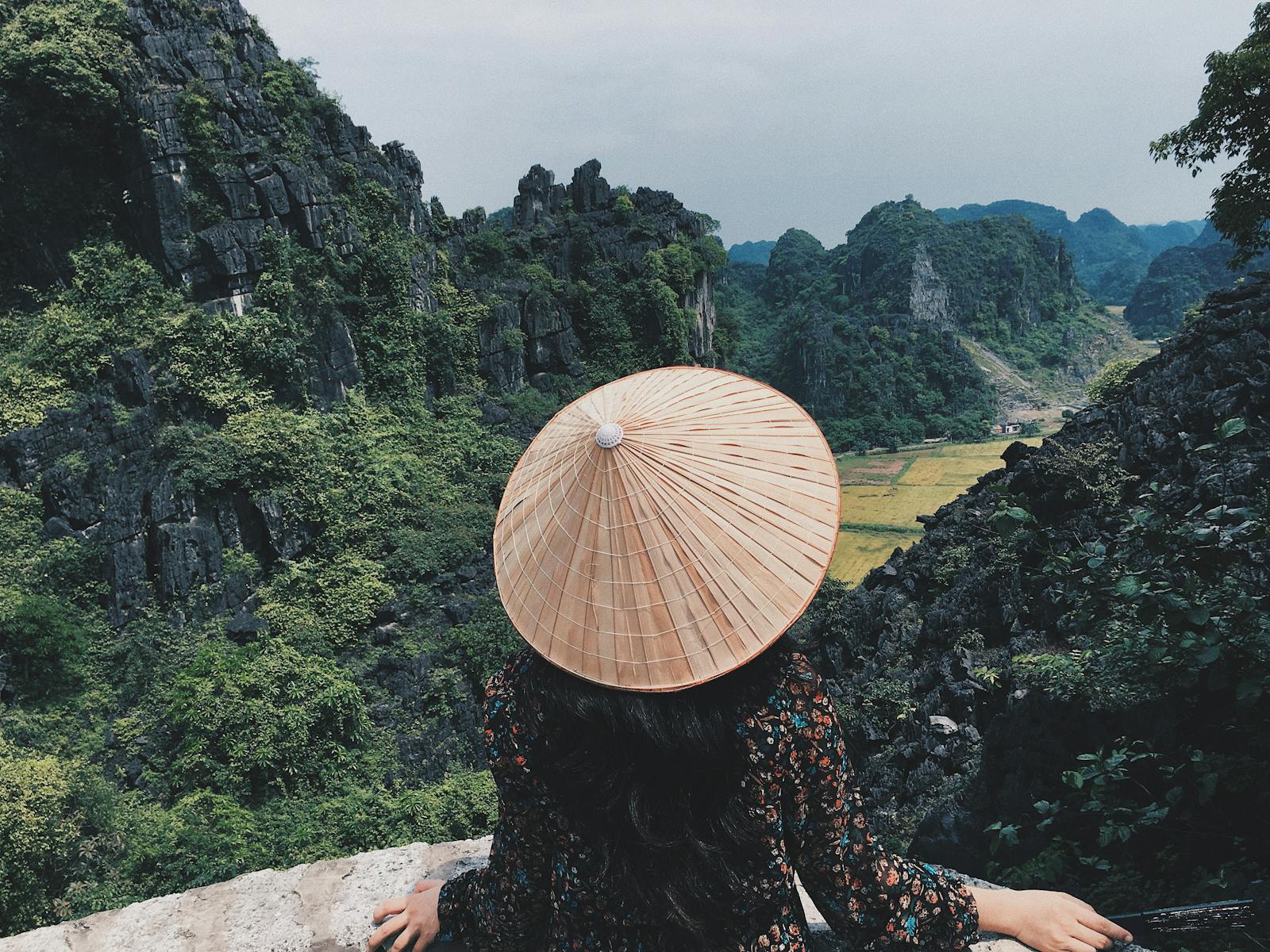 Woman in traditional hat overlooks stunning limestone cliffs in Ninh Binh, Vietnam.